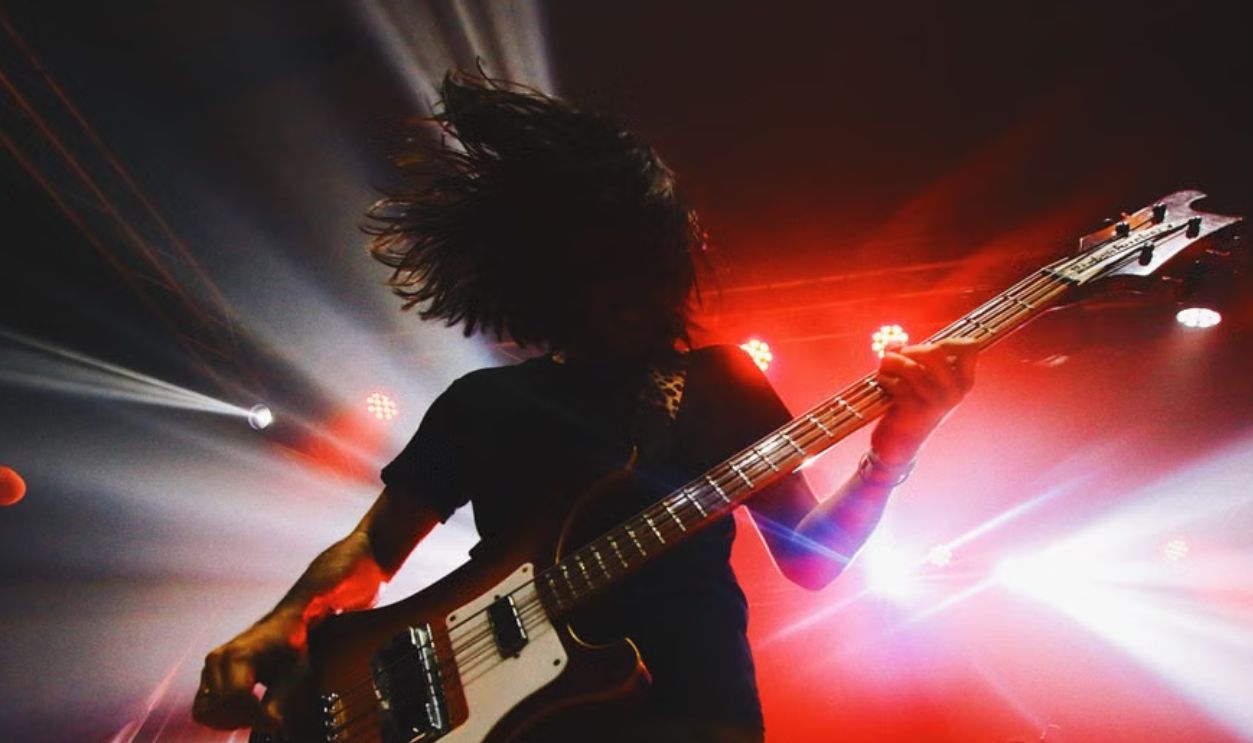Intense live rock concert capturing a bassist in action under vibrant stage lights