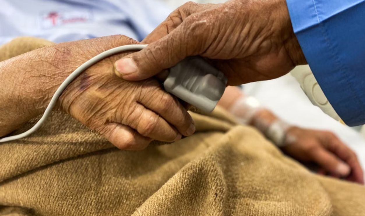 Senior patient's hand being comforted by a doctor's hand in a hospital setting, symbolizing care and support.