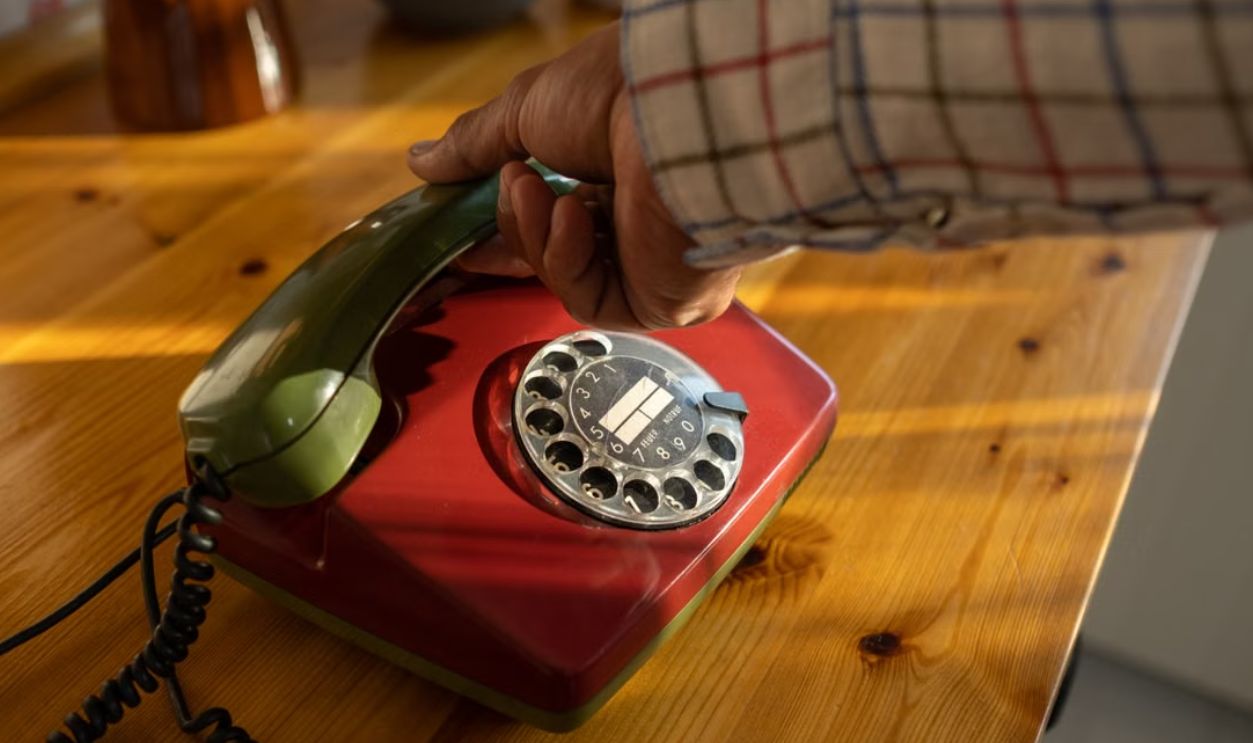 Close-up of a vintage rotary phone being held by a senior hand, evoking nostalgia