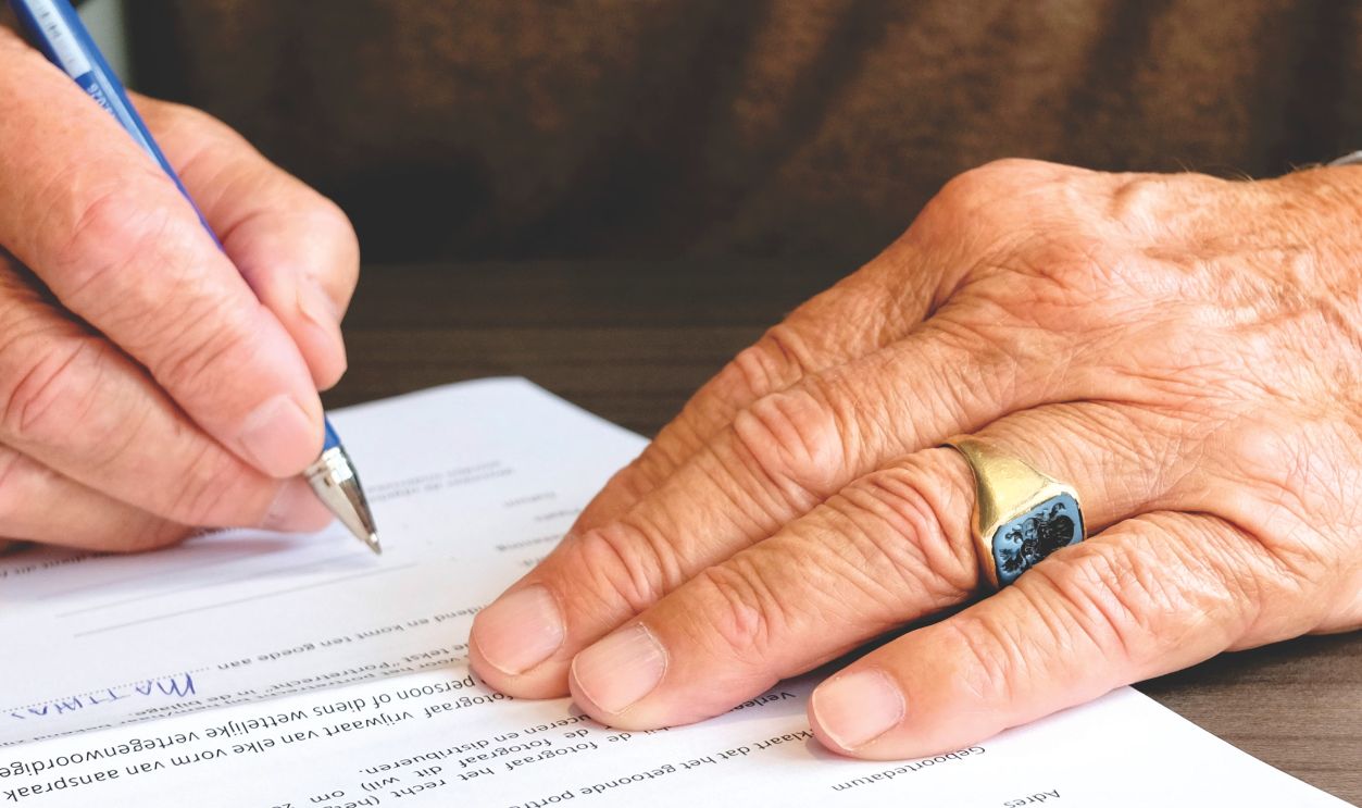 Close-up of a senior adult signing a legal document with a focus on hand and gold ring