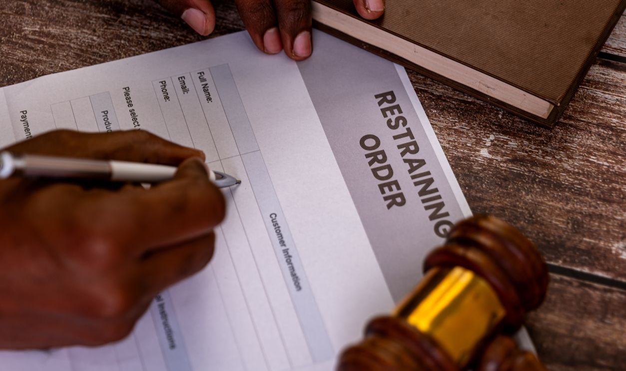Hands filling out a restraining order form with a gavel nearby. Legal protection, domestic violence, court order concept.