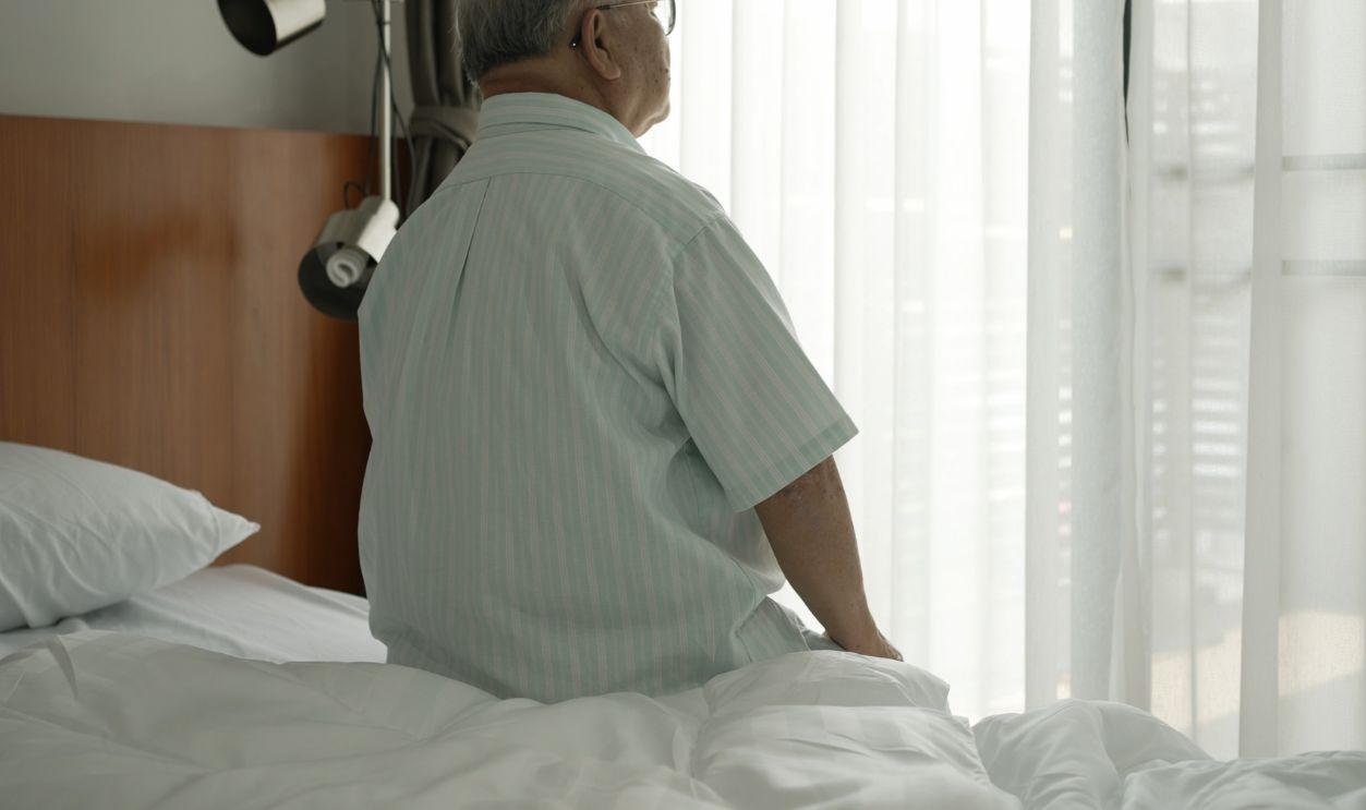 Asian senior old man uncle make up from bed in bedroom at morning and standing to open curtain for receive sunshine. Happy life after retired concept.