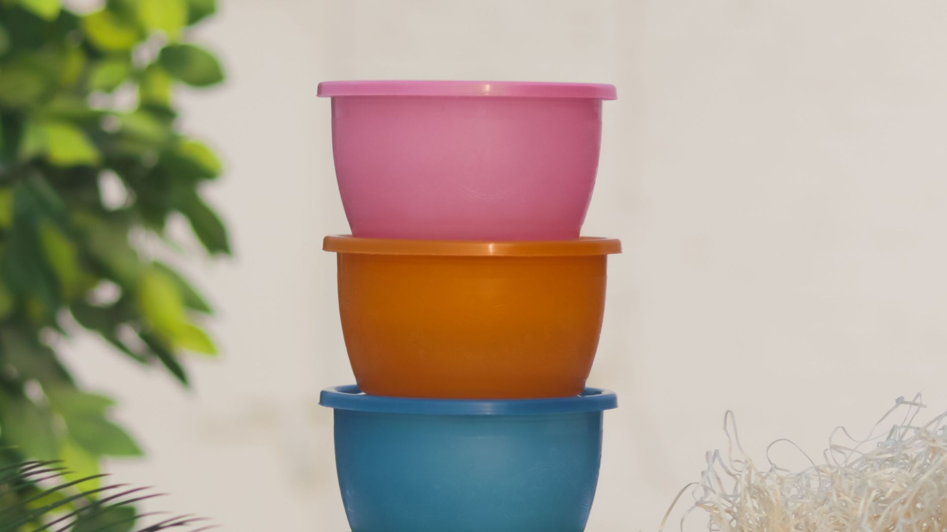 A vibrant stack of colorful plastic containers outdoors, surrounded by plants and straw.