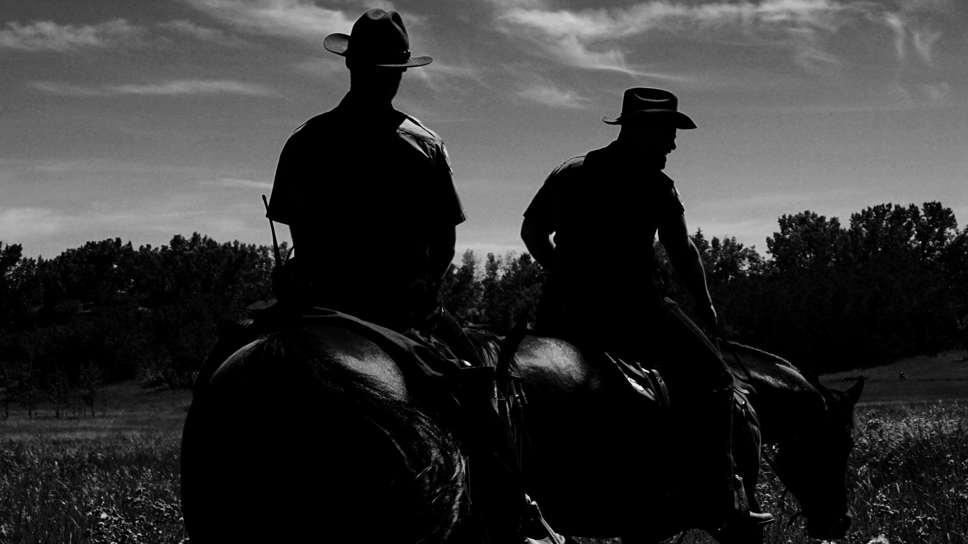Two cowboys riding horses through a field