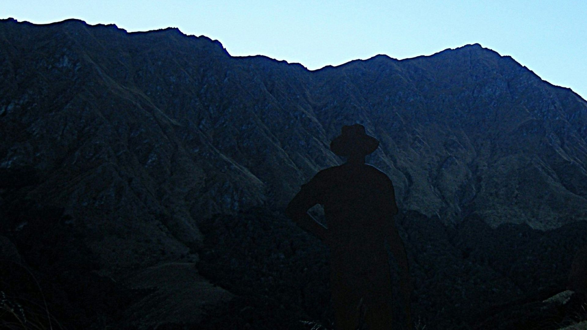 Two people in silhouette on a mountain trail against a clear blue sky