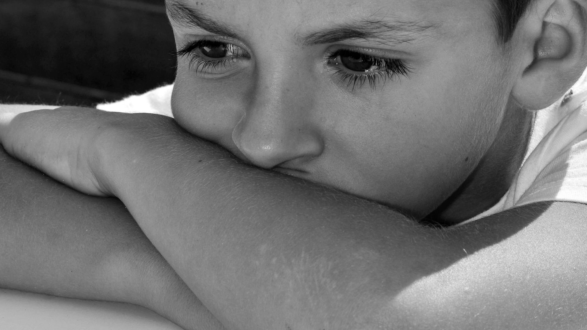 Thoughtful close-up portrait of a young boy wearing a hat, captured in black and white.