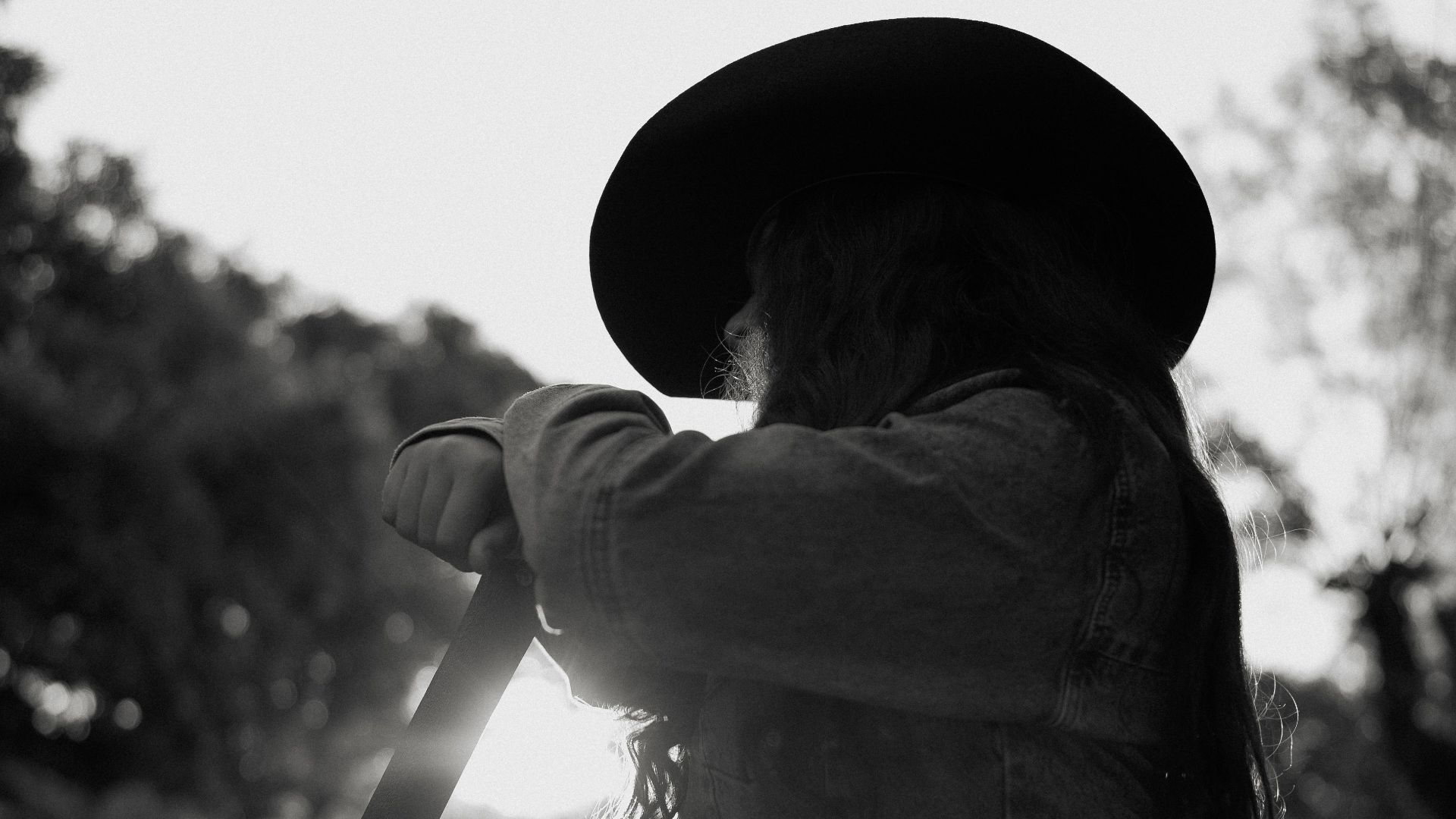 Black and white photo of a woman in a cowboy hat outdoors at sunset, casting a silhouette.