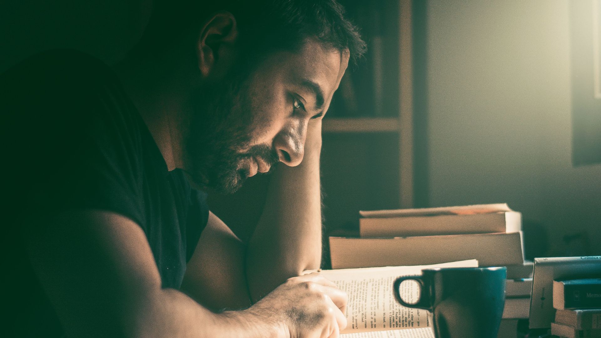 An adult man immersed in reading by the window in Madrid. Warm, focused study atmosphere.