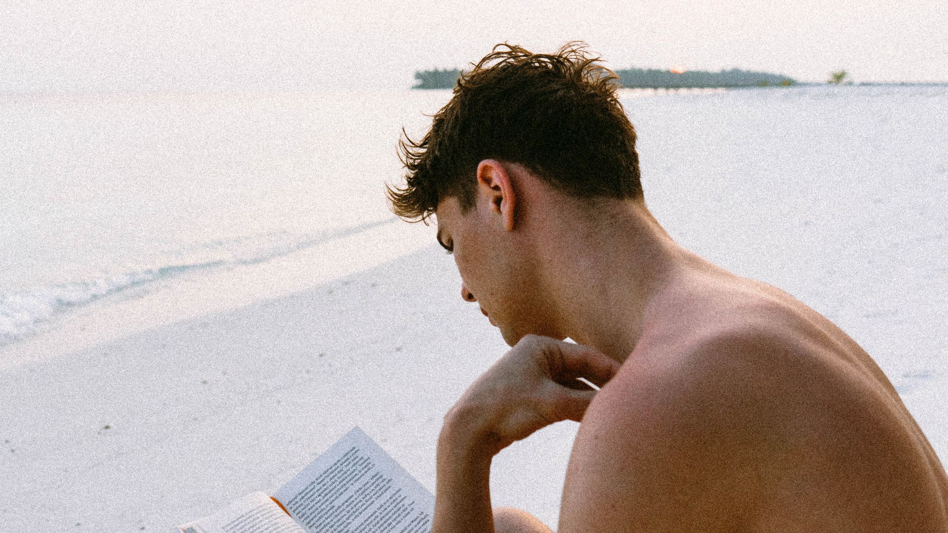 A man enjoys reading a book on a serene Maldives beach, capturing the essence of relaxation.