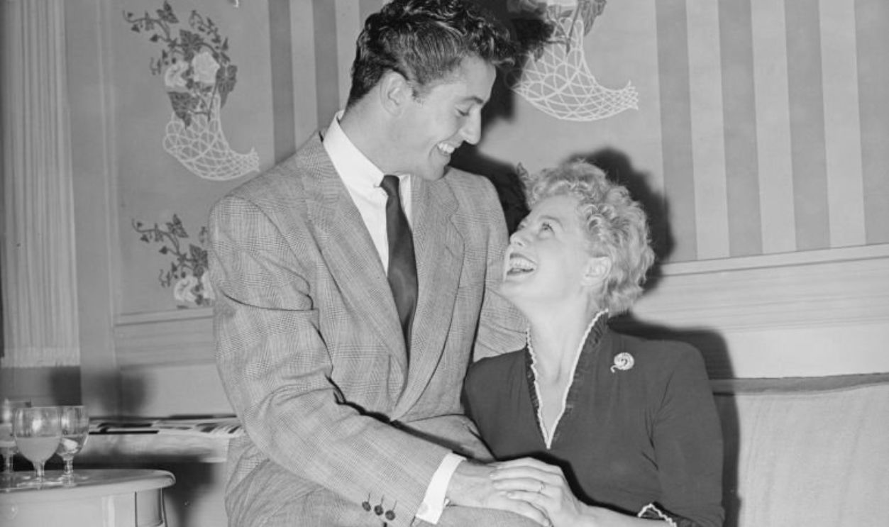 27th September 1951: Film star Farley Granger perches on the arm of a sofa next to Shelley Winters, his co-star in George Beck's 'Behave Yourself!'. 