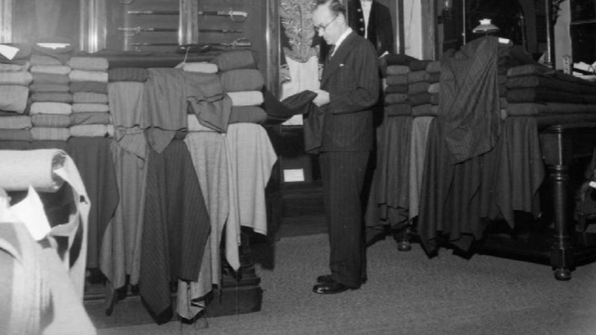 Savile Row- Tailoring at Henry Poole and Co., London, England, UK, 1944
A member of staff at Henry Poole and Co. examines fabrics in the showroom on Savile Row.  Behind him can be seen a large cabinet in which are displayed various swords and several mili