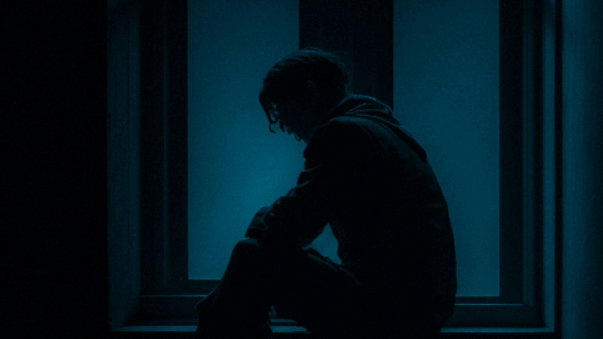 a man sitting on a window sill in the dark