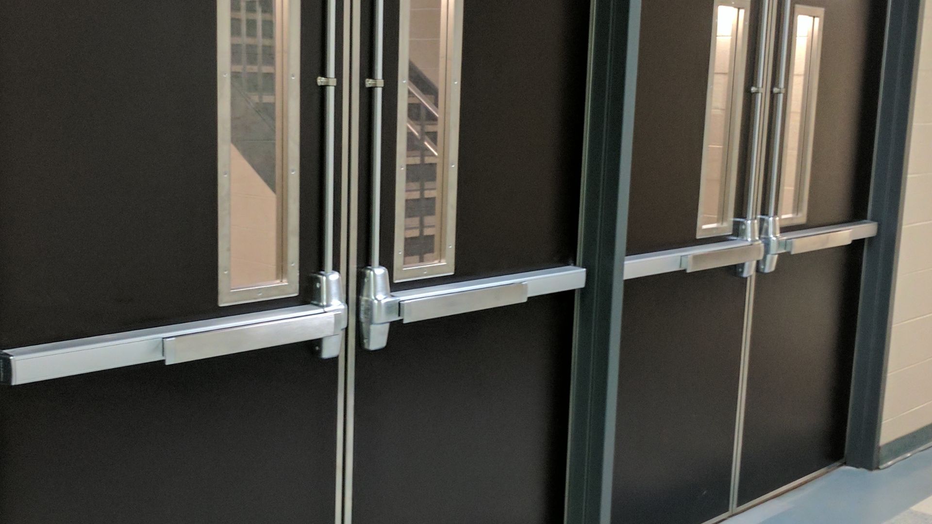 A set of doors in a US school fitted with push bars (aka. panic or crash bars) and upper Pullman latches.