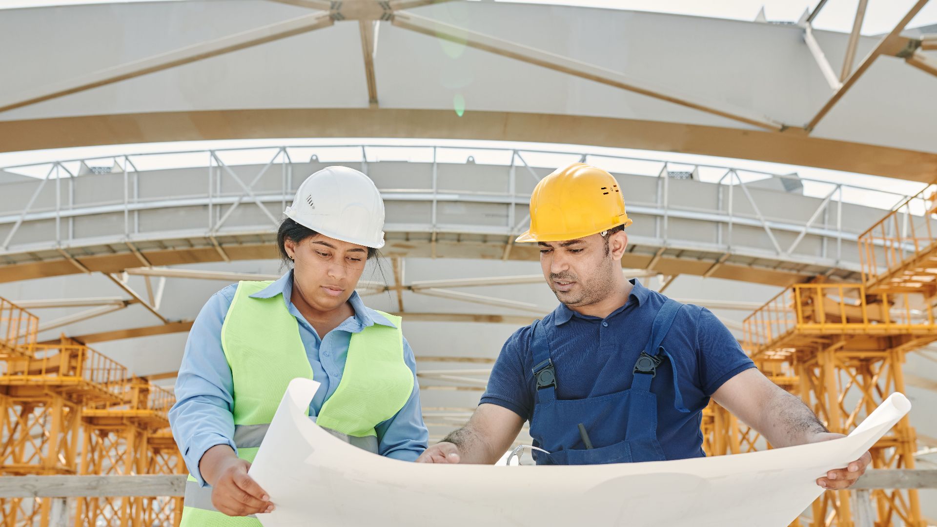 Male and female engineers discussing blueprints at a construction site, promoting teamwork and planning.