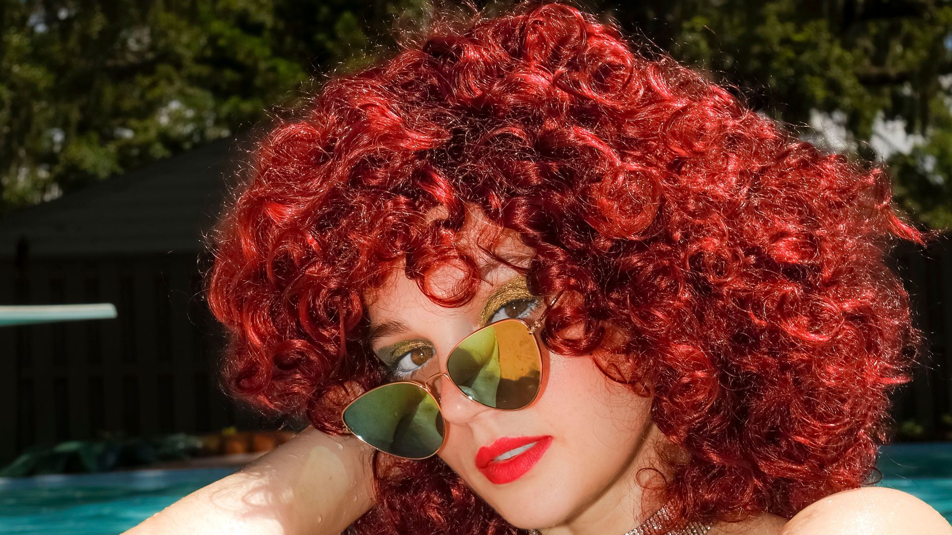 Vibrant red-haired woman in sunglasses enjoying the sun by the pool.