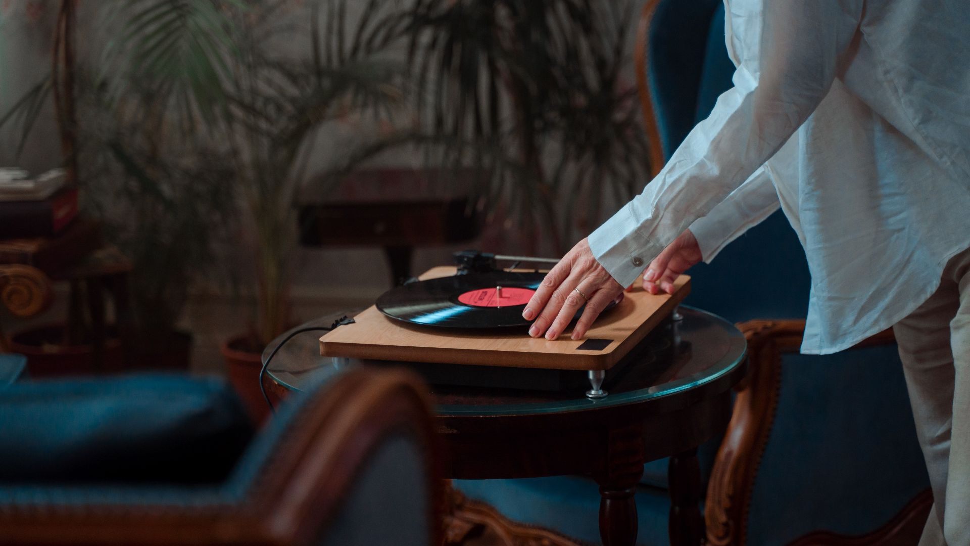 A person adjusting a vinyl record on a turntable in a cozy indoor setting.