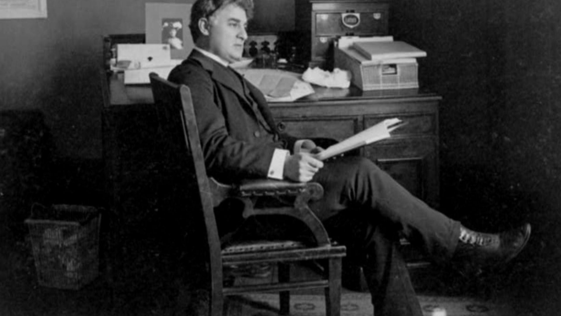 David Belasco, full-length portrait, seated at desk, facing right.