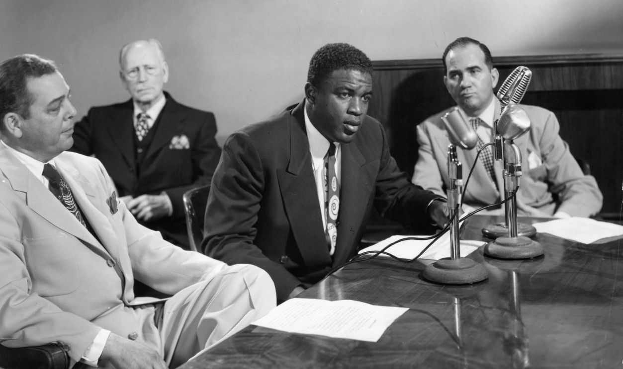 Jackie Robinson sitting at a table with microphones sitting in front of him in a scene from the film 'The Jackie Robinson Story', 1950. 