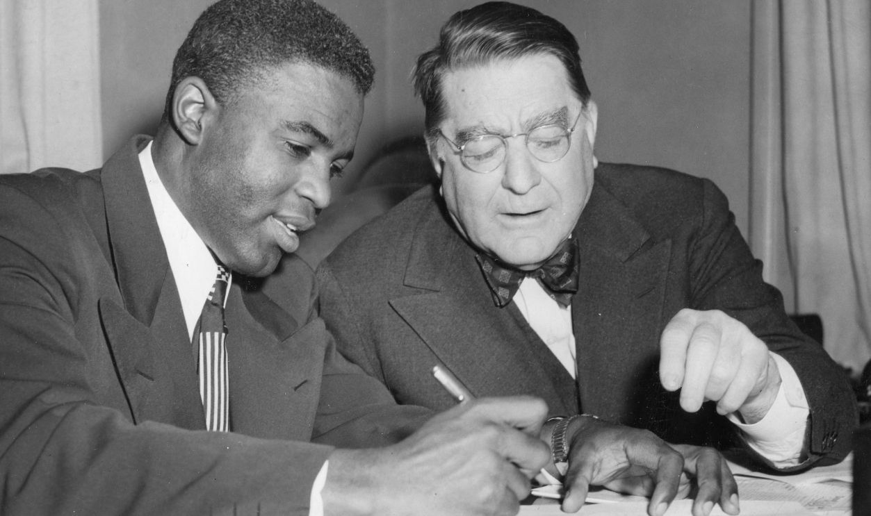 American athlete and second baseman for the Brooklyn Dodgers Jackie Robinson signs his contract for team president Branch Rickey, Brooklyn, New York, New York, January 1950.