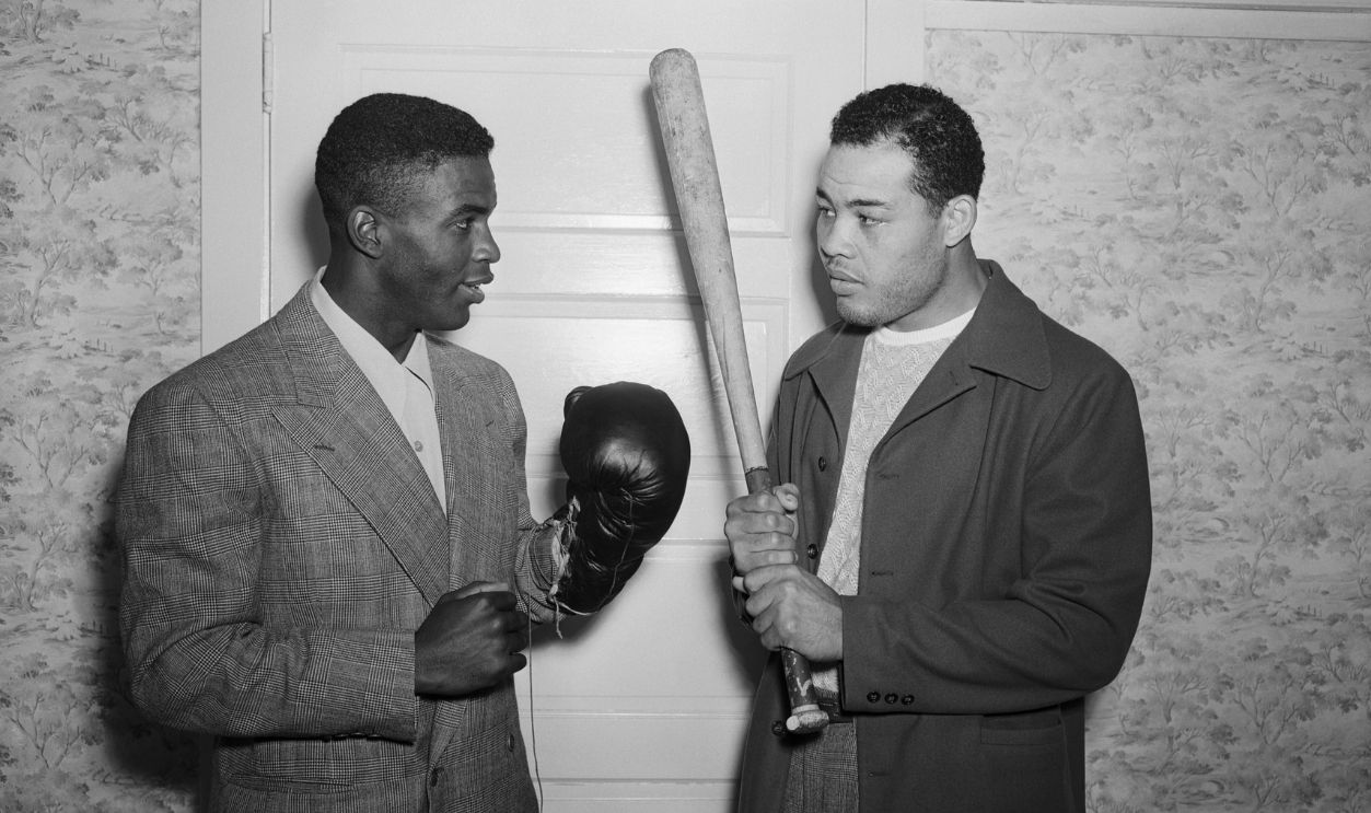 Heavyweight champion Joe Louis (r) and Jackie Robinson,ex-UCLA football star and former U. S. Amry Leiutenant,who has achieved the distinction of being the first Negro signed up by a club in organized baseball,try the weapon of each other's trade at Louis' Pompton Lake, NJ, training camp,June 14. Robinson plays with the Montreal Club of the International Legaue, a class AA circuit. In five days,Louis defends his title against Billy Conn at the Yankee Stadium,New York.