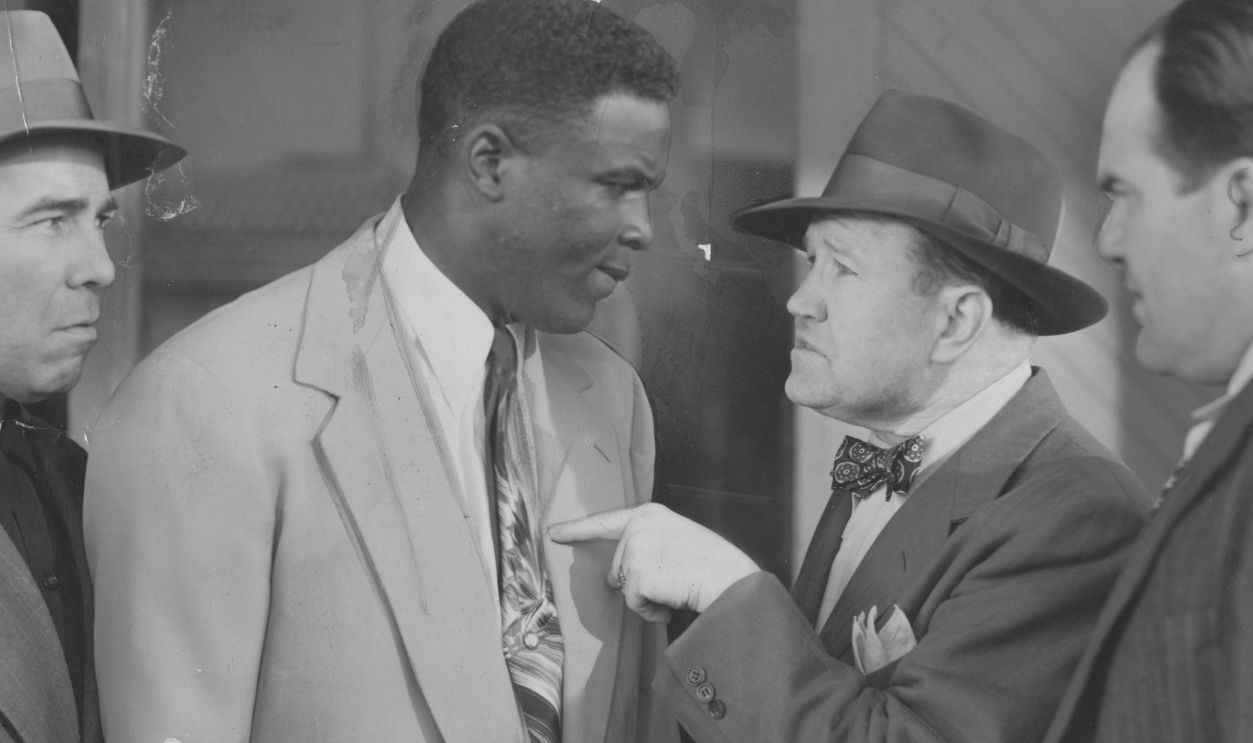 American baseball player Jackie Robinson (1919 - 1972) of the Brooklyn Dodgers and three men in suits, 1948.