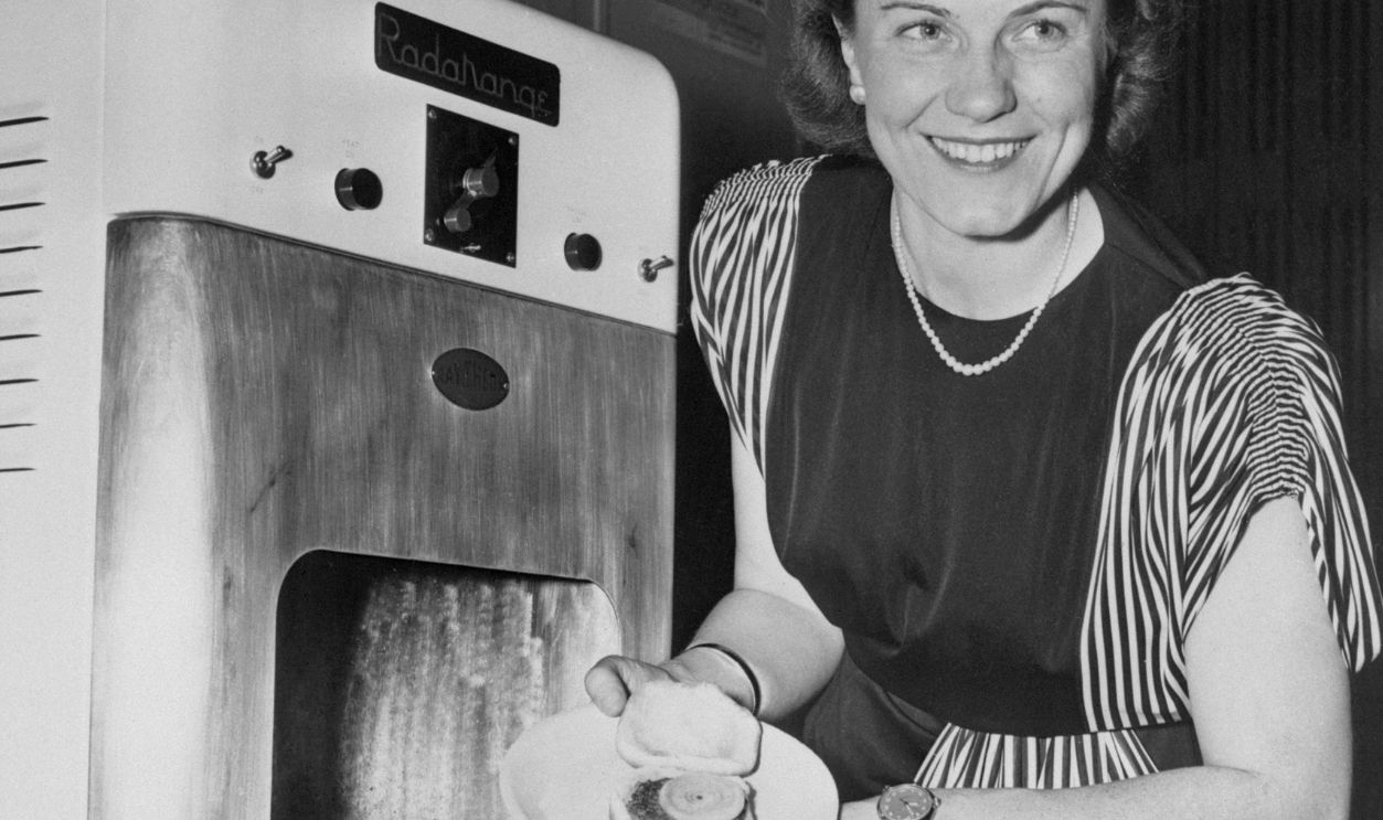 New York: Anita Howarth is shown removing a well cooked hamburger sandwich, fifteen seconds after it was placed in the new Raytheon Radarange, during a demonstration today at the engineering societies auditorium in New York City. The new machine, as easy to operate as an ordinary electric range, utilizes the Raytheon Magnetron, the very heart of radar, from which radio frequency energy waves are concentrated directly into the "oven." This amazing new machine can cook a half of a small sized fresh chicken in 4 minutes and a frankfurter in ten seconds.