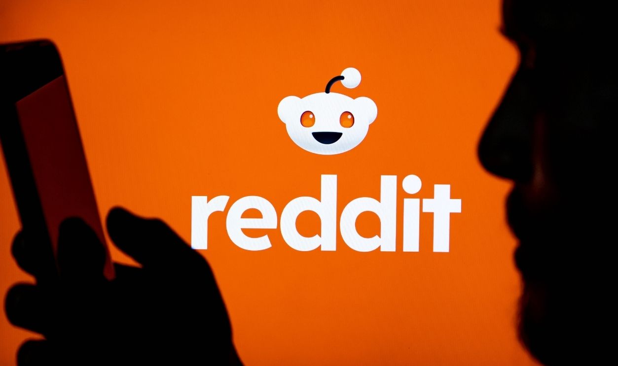 Silhouette of a person using a smartphone with the reddit logo displayed on a large screen in the background. India on May 05, 2026