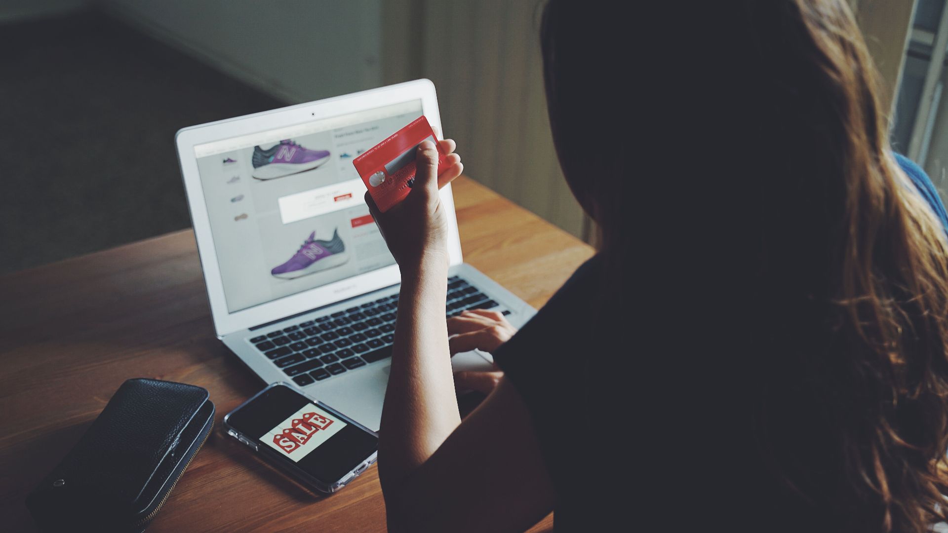 A woman shops online using a laptop and credit card on a wooden table.