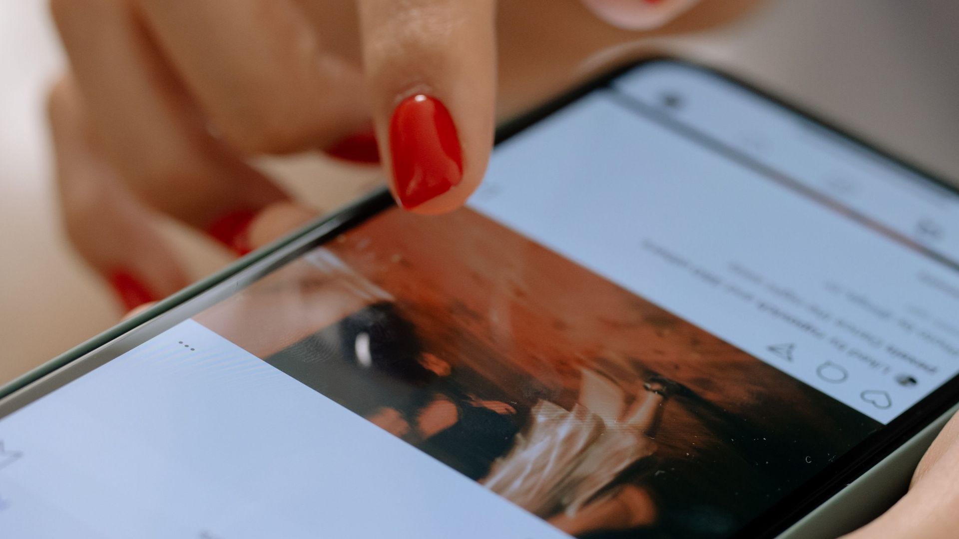 A woman with red nails using a smartphone, navigating a social media app.