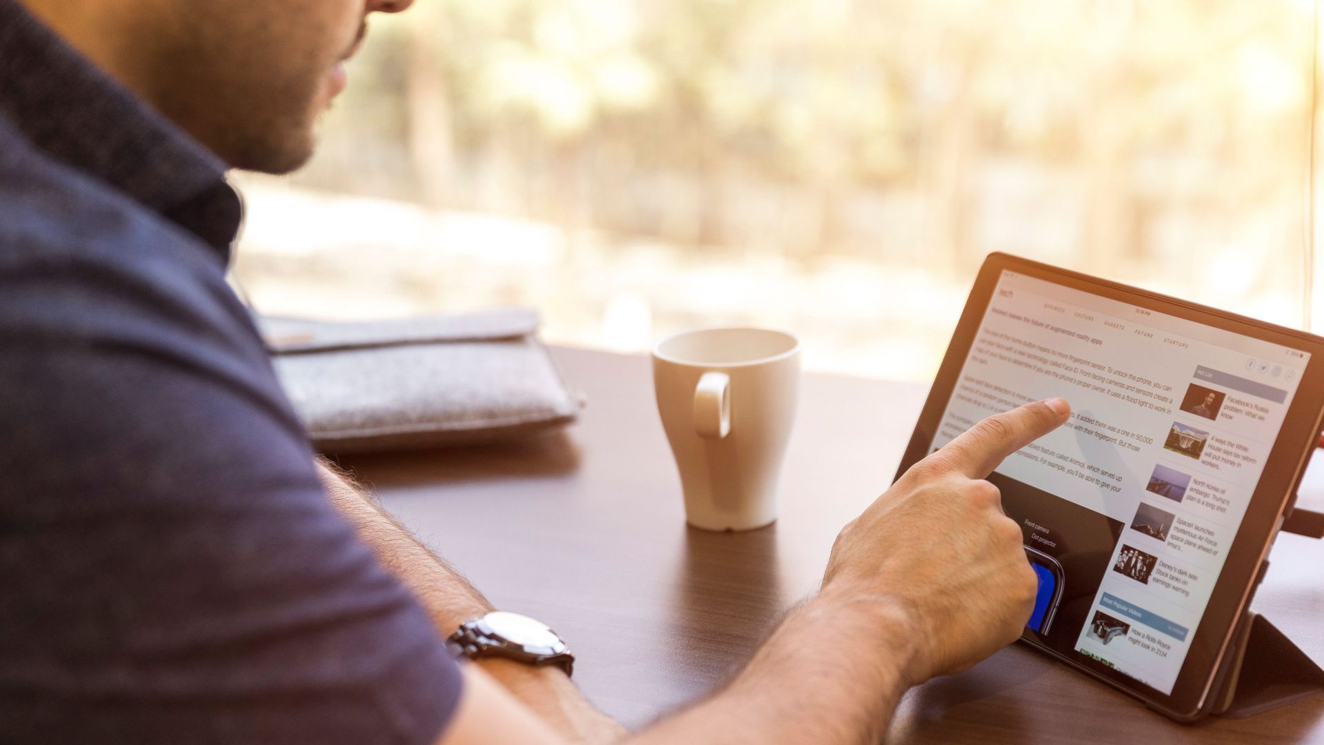 Adult man browsing a tablet with coffee indoors during the day.