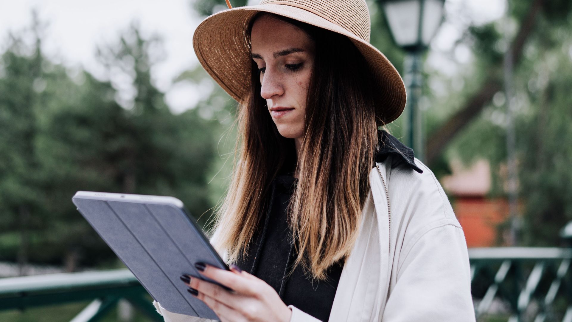 A woman stands on a bridge using a tablet, enjoying leisure time outdoors.