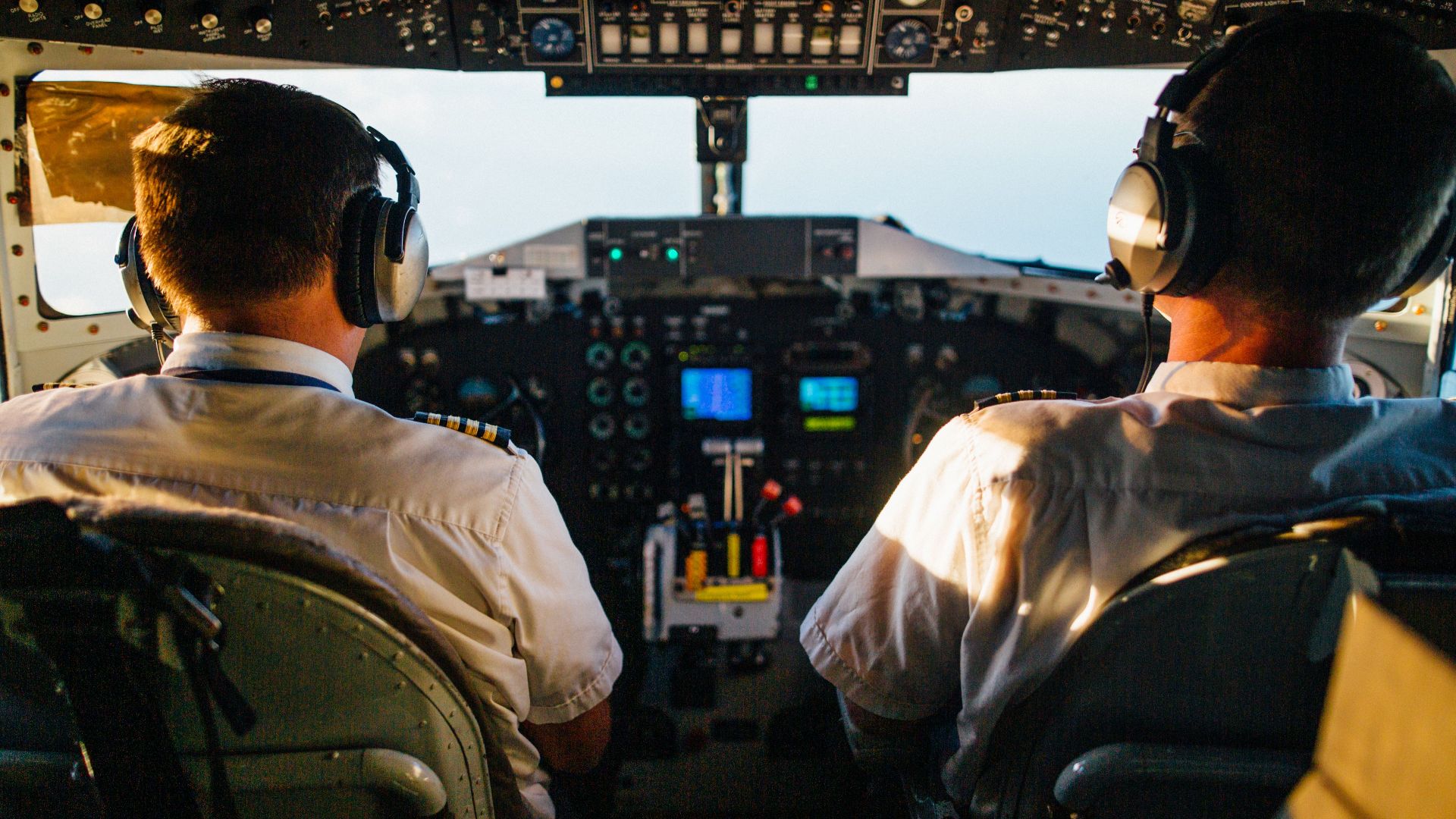 Two pilots in cockpit navigating airplane at high altitude, daylight