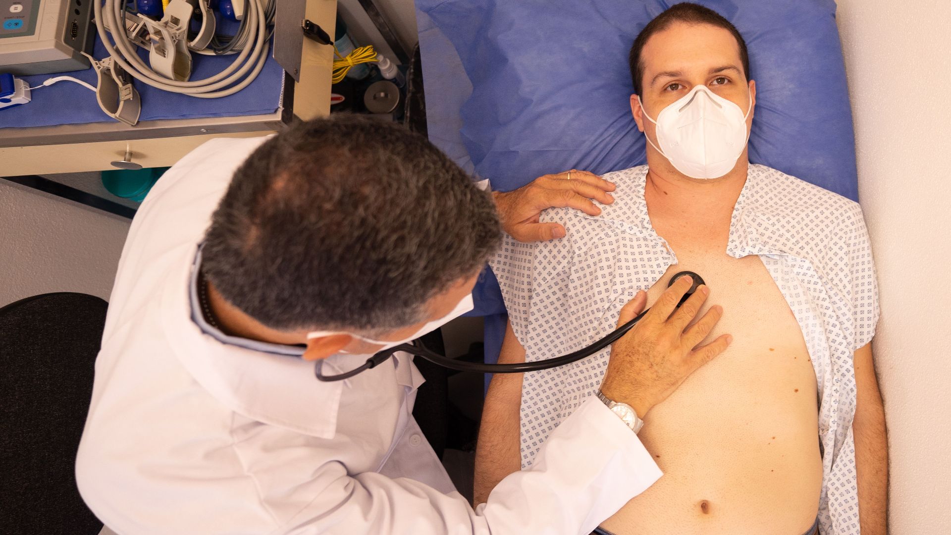 Doctor in protective mask examines patient with stethoscope in medical clinic.
