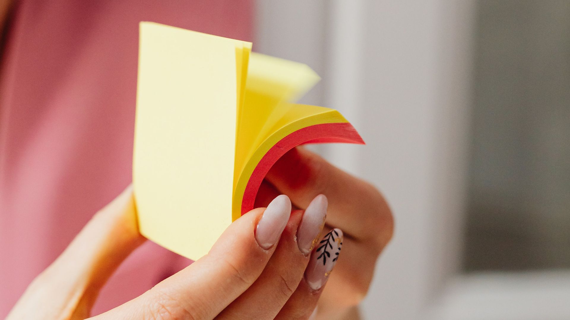 Focused woman with manicured nails holding colorful sticky notes indoors.