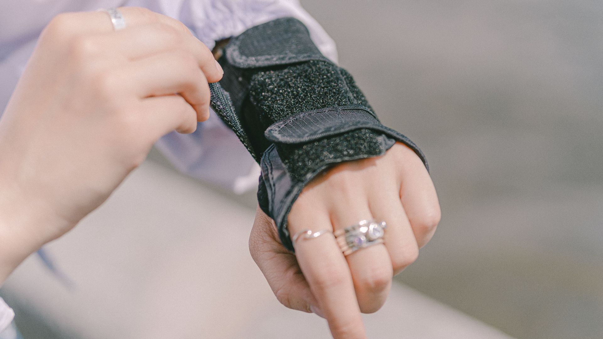 Detailed shot of a hand with rings adjusting a wrist brace, showcasing protection and style outdoors.