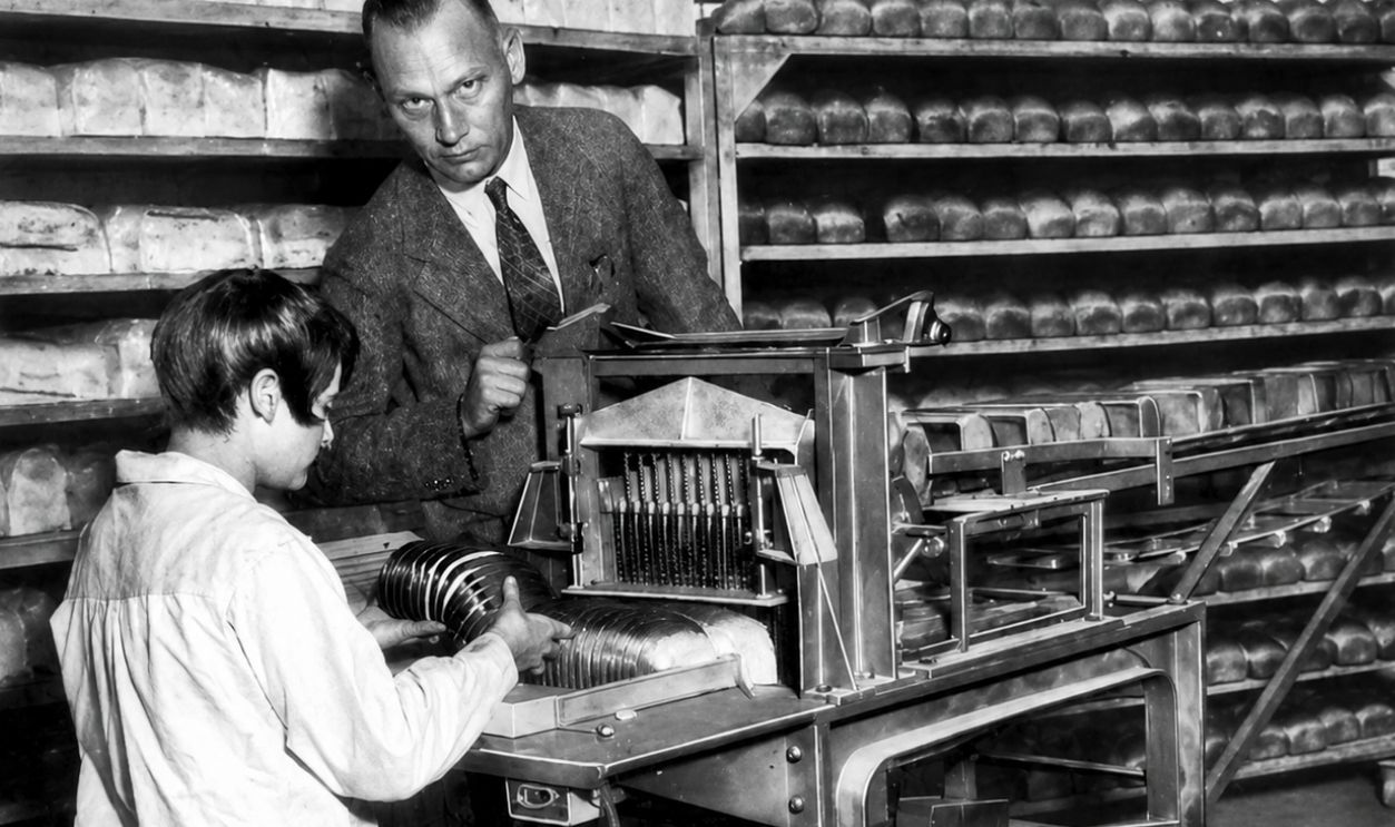 1930 photograph from the magazine Popular Science with the caption, "The new electric bread slicing machine at work in a St. Louis, Mo. bakery. The operator is holding one of the sliced loaves." The accompanying article does not identify the bakery but this may have been the machine invented by Otto Frederick Rohwedder of Davenport, whose 2nd slicing machine was purchased by Gustav Papendick of Papendick Bakery Company in St. Louis who worked out a process to wrap the sliced loaf automatically. 