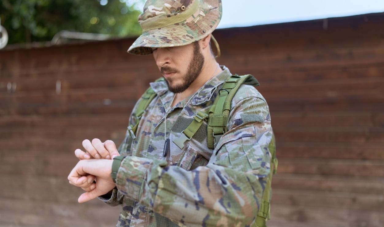 Young hispanic man wearing soldier uniform looking watch at park