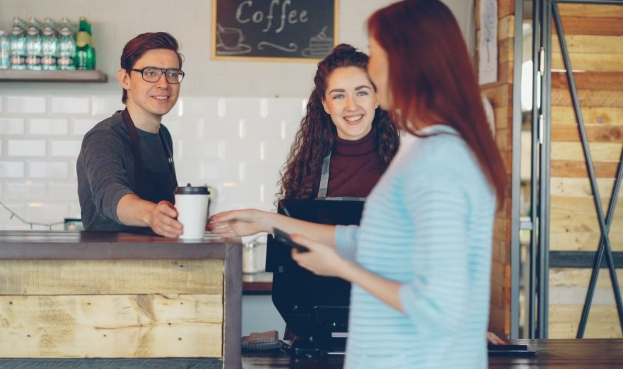 Barista hands coffee to a customer in a cozy cafe setting