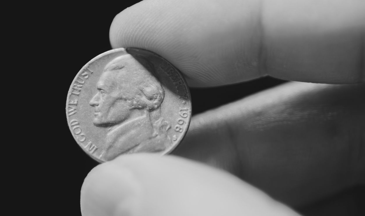 Close-Up of a Hand Holding a Nickel Coin Against a Dark Background