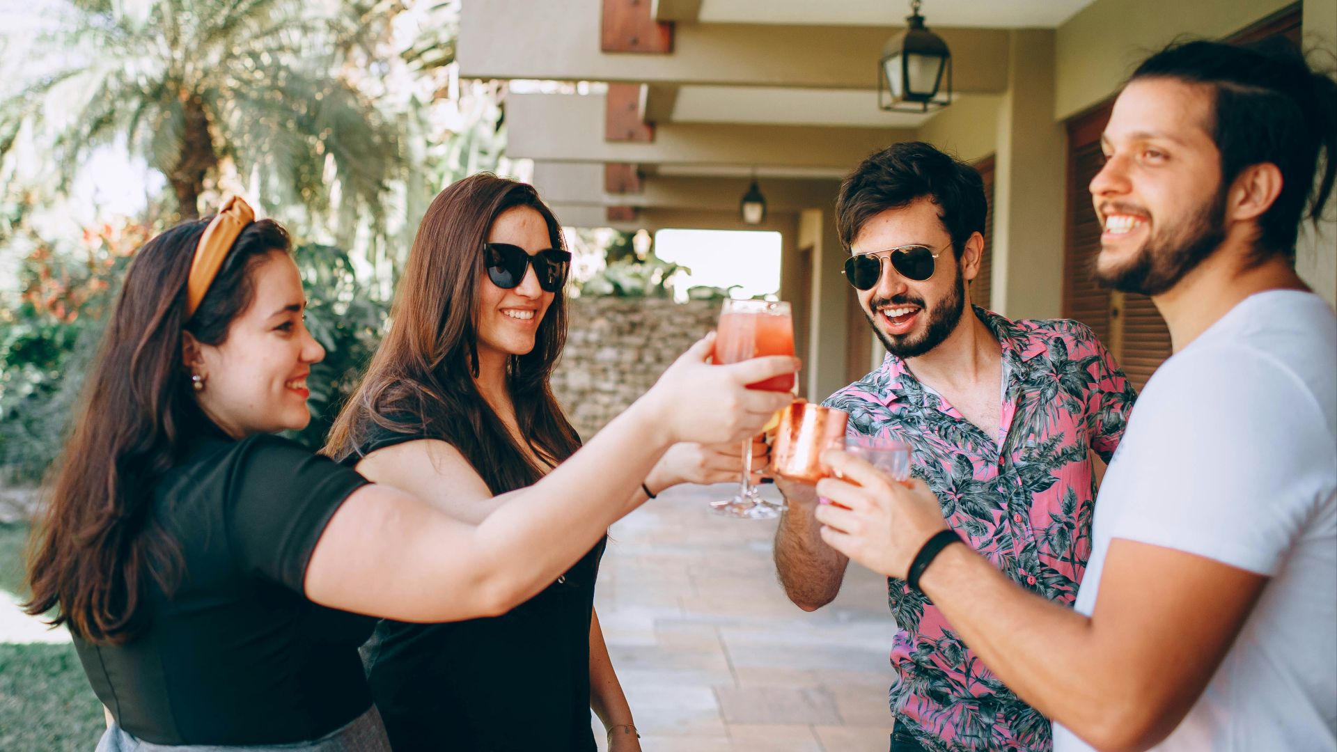 man in black t-shirt holding drinking glass beside woman in floral dress holding drinking glass