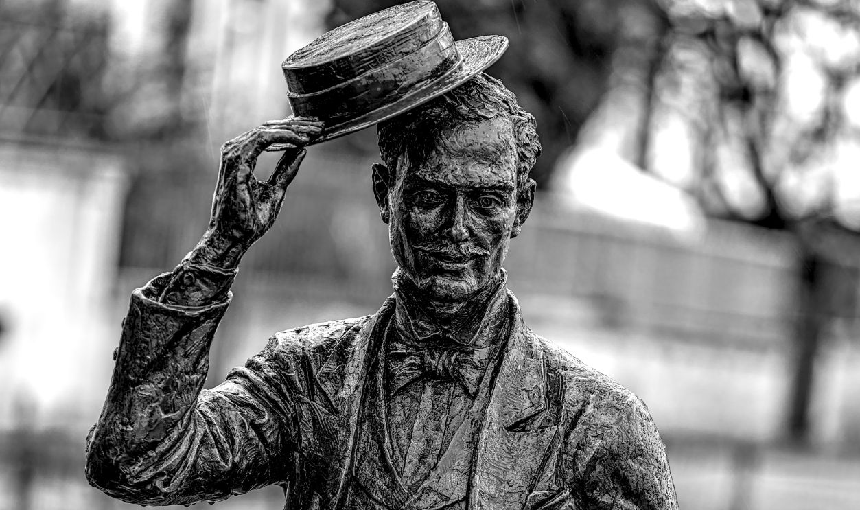 Elegant bronze statue of a man in a suit tipping his hat, captured in black and white.