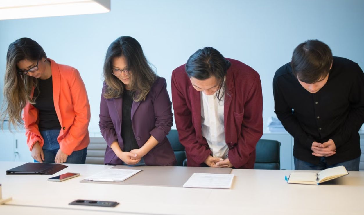 Business meeting with a diverse team bowing in respect, symbolizing cultural cooperation.