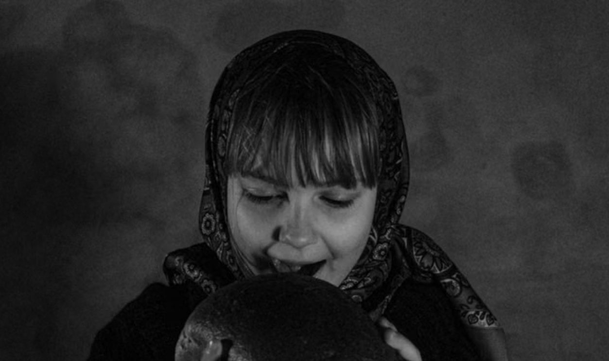 Black and white portrait of a girl eating bread, conveying hunger.