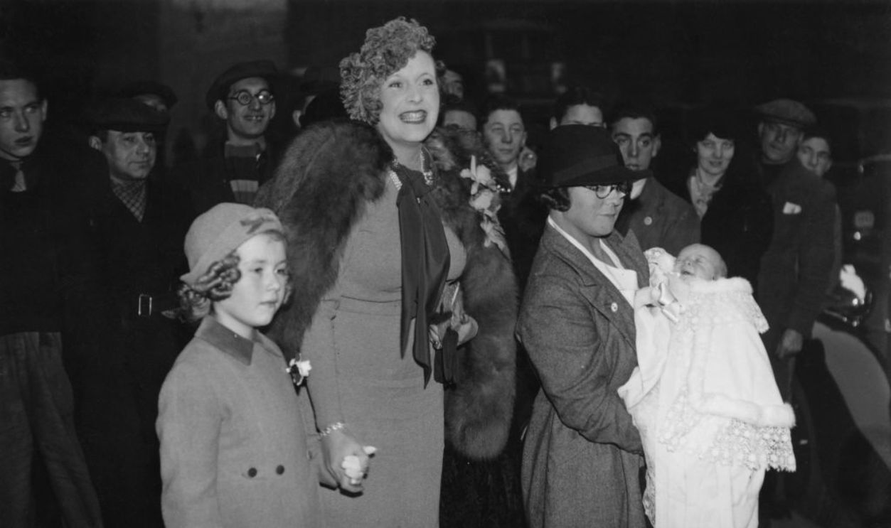 Novelist Barbara Cartland, with her daughter Raine at the christening of her son Ian Hamilton McCorquodale, 24th November 1937. The ceremony took place at the Church of St Ethelburga the Virgin, Within Bishopgate, London.