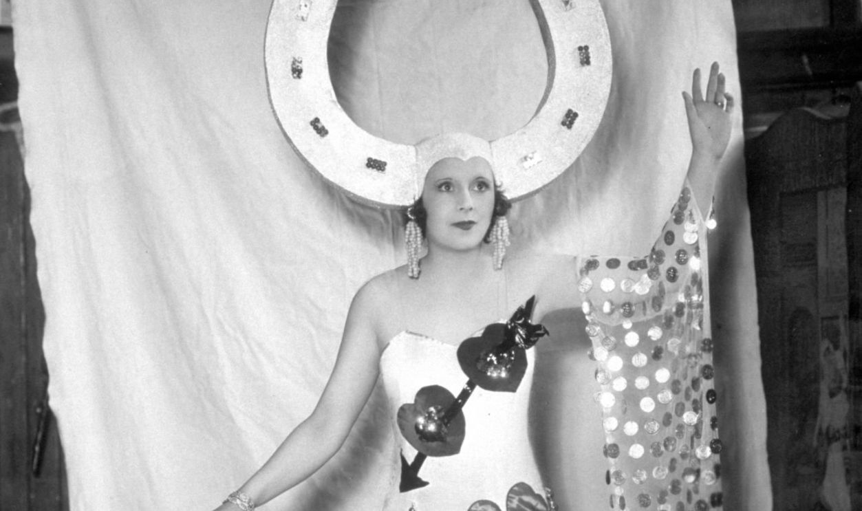 1st November 1930: Barbara Cartland (1901 - 2000) wearing a huge horseshoe on her head as 'Good Luck' in the 'Pageant of the Superstitions' at the Haymarket Theatre, London.