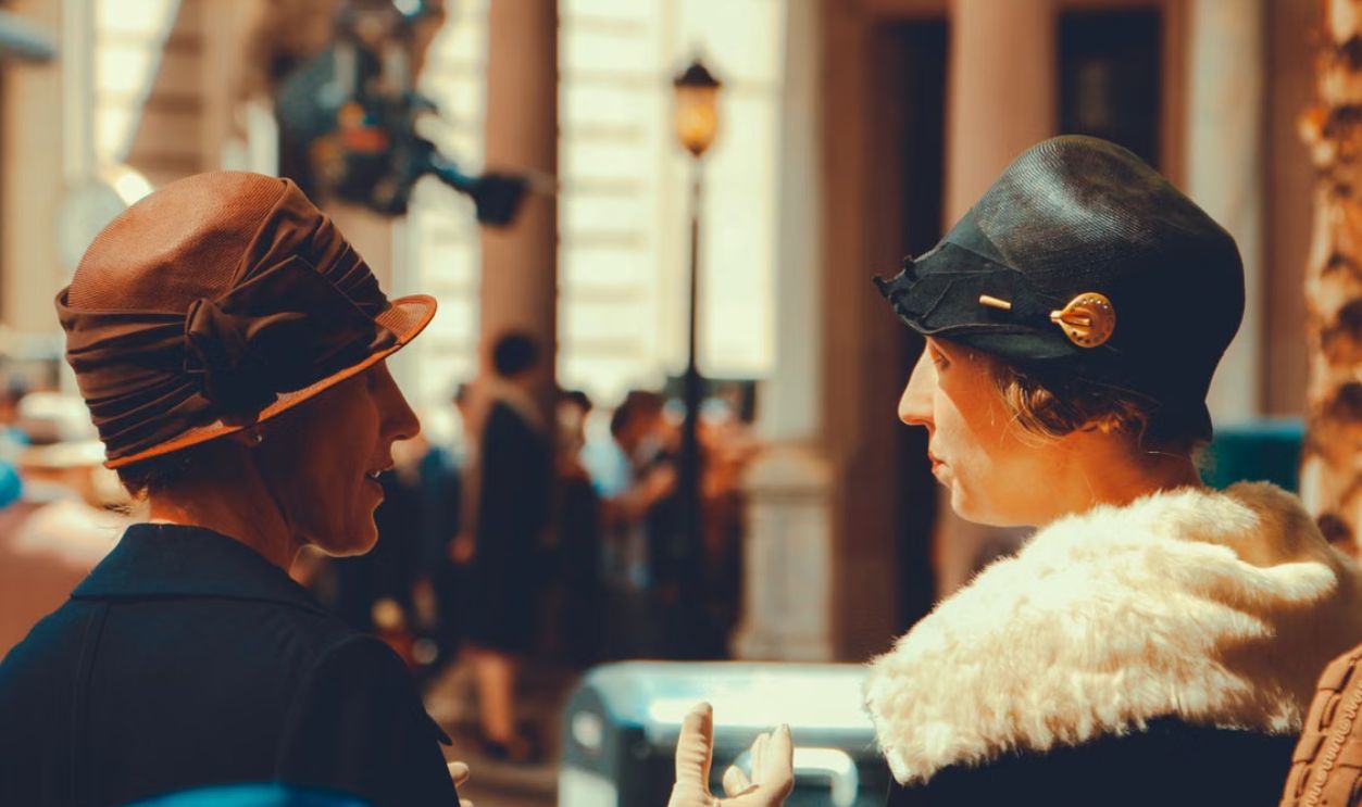 Two women in vintage attire converse outdoors in New York City, showcasing retro fashion.