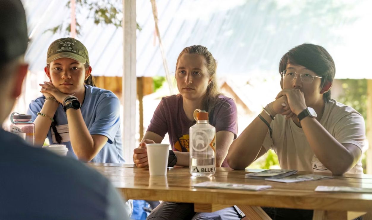 Three young people attentively listening at a table.