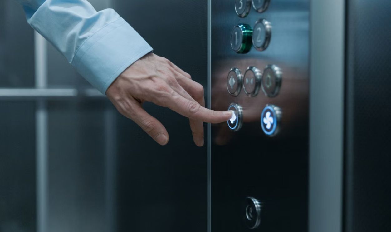 A person pressing an elevator button in a modern building, highlighting technology and urban life.