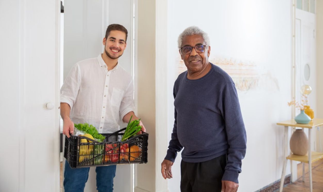 Senior man receiving fresh produce from a young volunteer indoors, promoting community support.