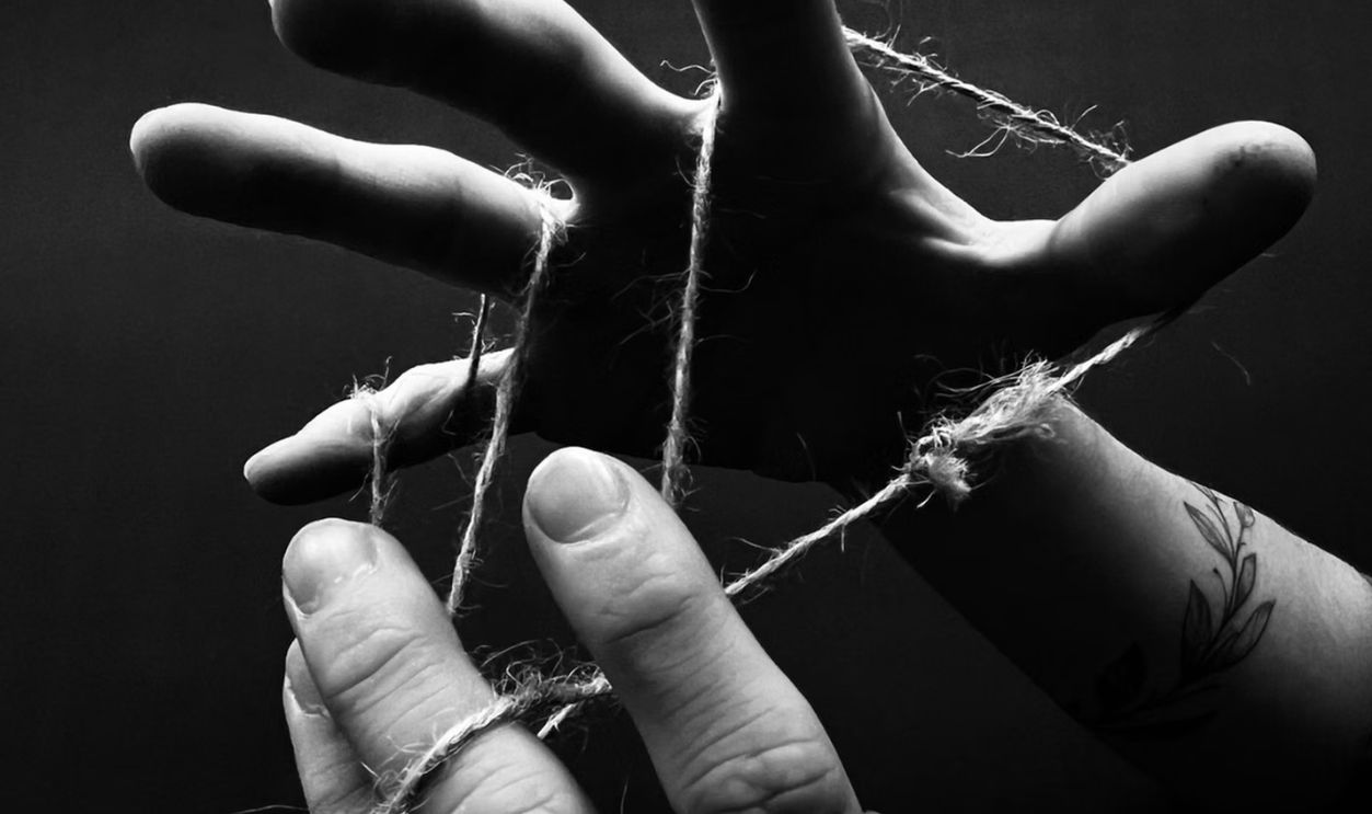 Artistic black and white photograph of hands tangled in string playing cat's cradle
